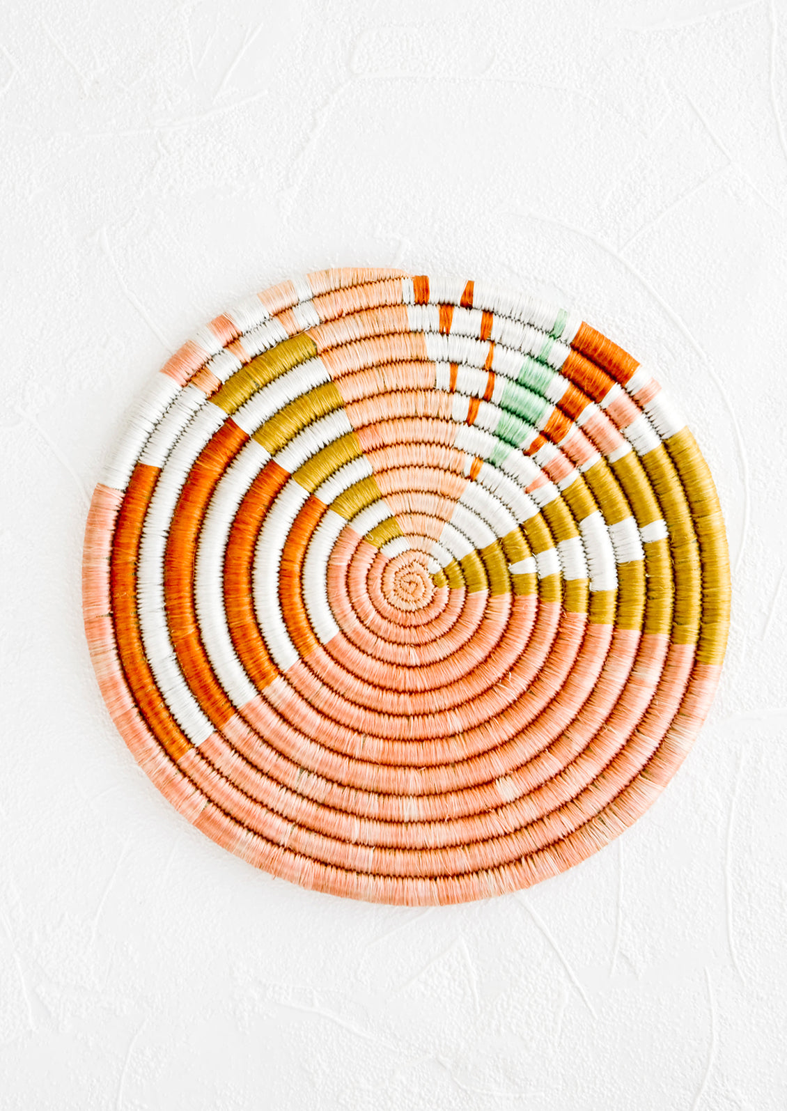 Colorful round trivet made from dyed raffia in a geometric pattern and pastel hues