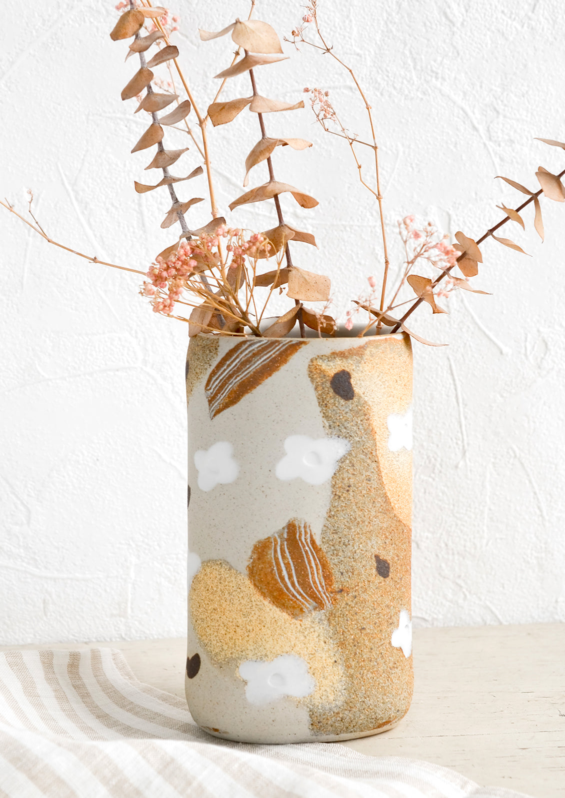 An oval shaped vase made from sandy clay with white and brown inlay detailing.