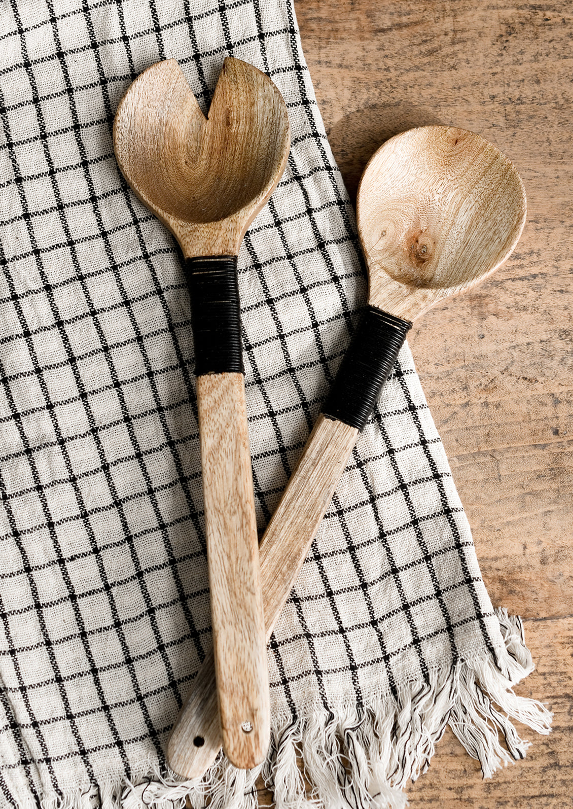 A pair of wooden salad servers with decorative black wire wrapping on handle.