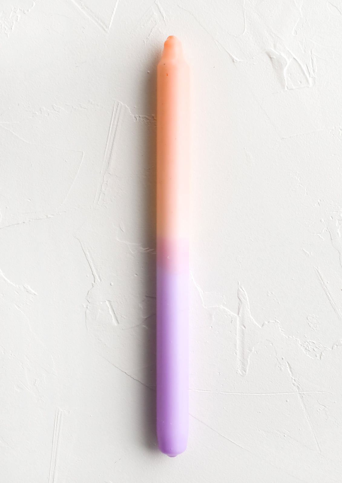 A straight taper candle in peach and lilac.