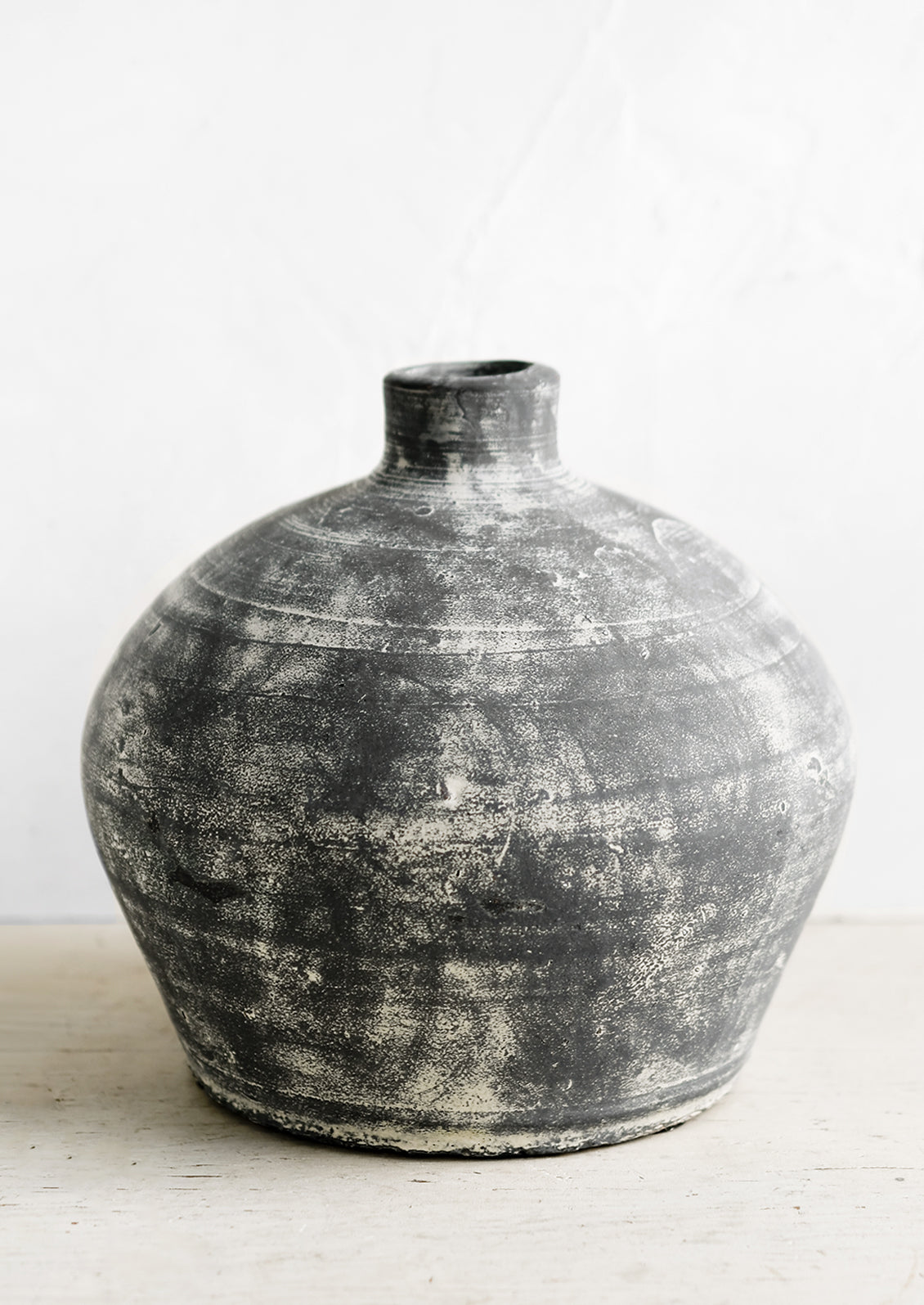 A distressed black clay vase with narrow opening.