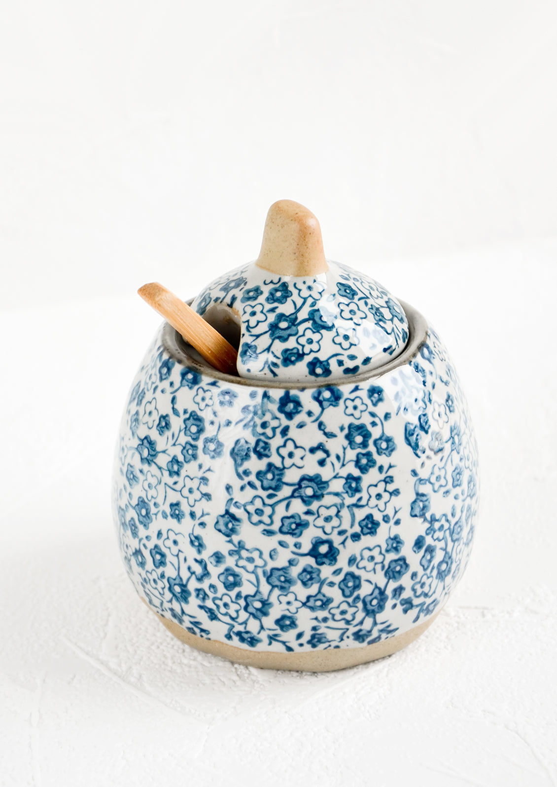 A lidded sugar jar with included spoon made of ceramic in grey with blue ditsy floral print.