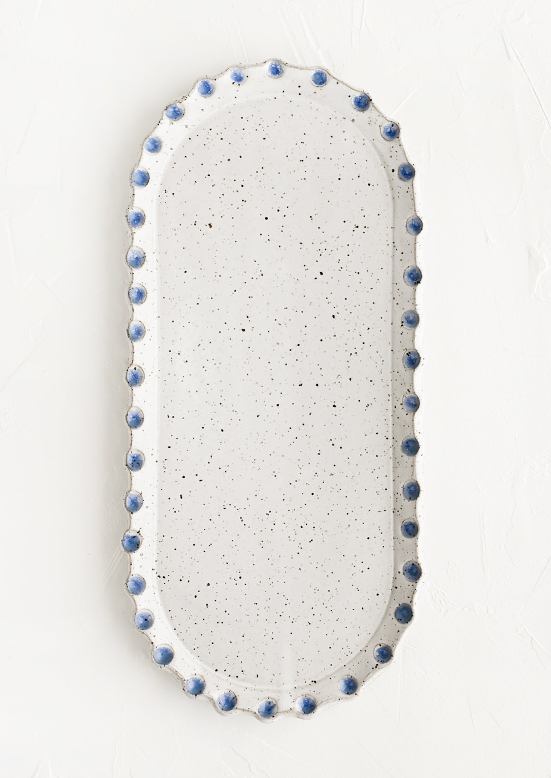 An oblong, oval shaped ceramic platter with blue dot imprint border.