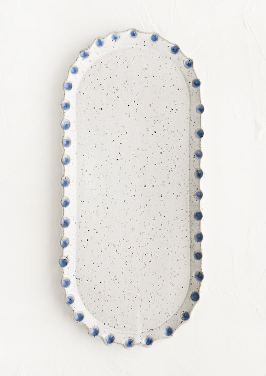 An oblong, oval shaped ceramic platter with blue dot imprint border.