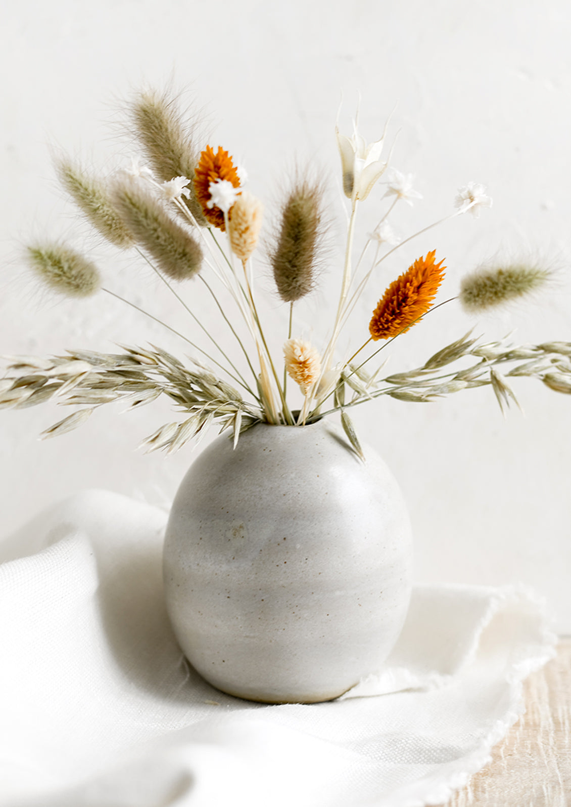 A bud vase holding dried flower arrangement.