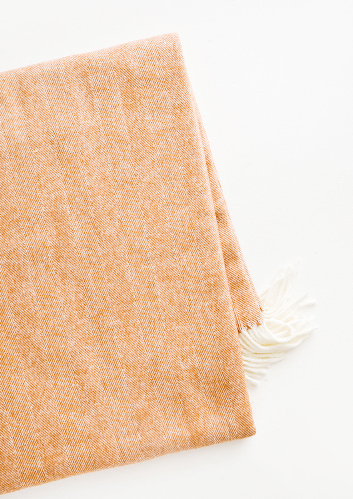 Soft blanket in copper colored herringbone weave. Ivory tassel trim at ends.