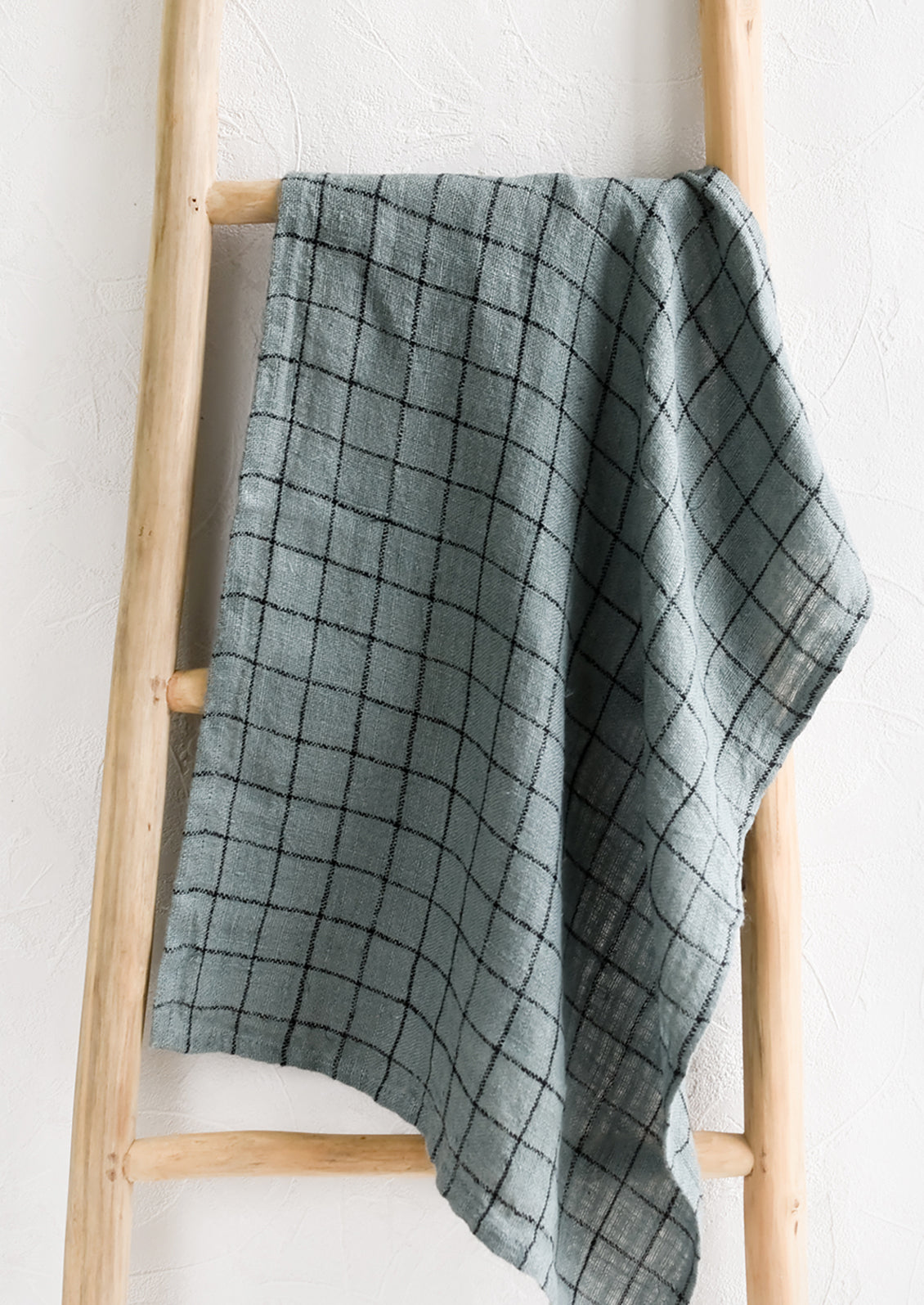 A woven tea towel in dusty blue with black grid pattern.