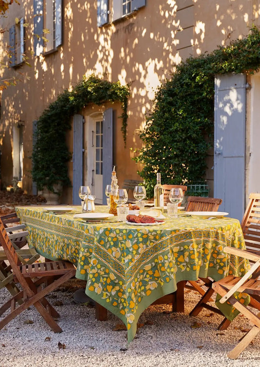 A yellow and green floral print tablecloth on a table set for dining, placed in a patio setting.