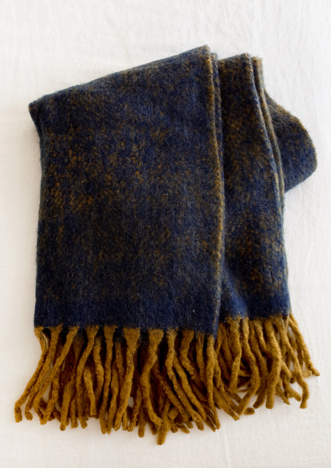 A fuzzy mohair-like blanket in navy and mustard with mustard tassel trim.
