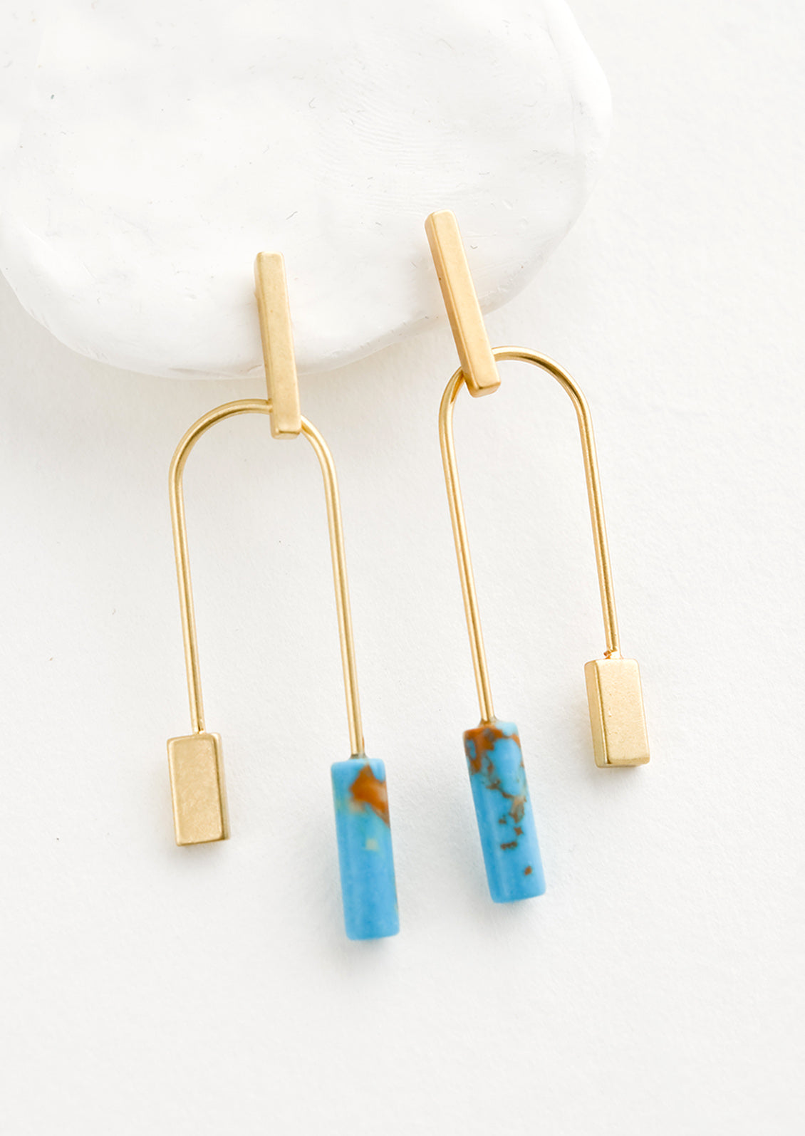 A pair of gold earrings with bar shaped top and arched bottom with turquoise gemstone on one side.
