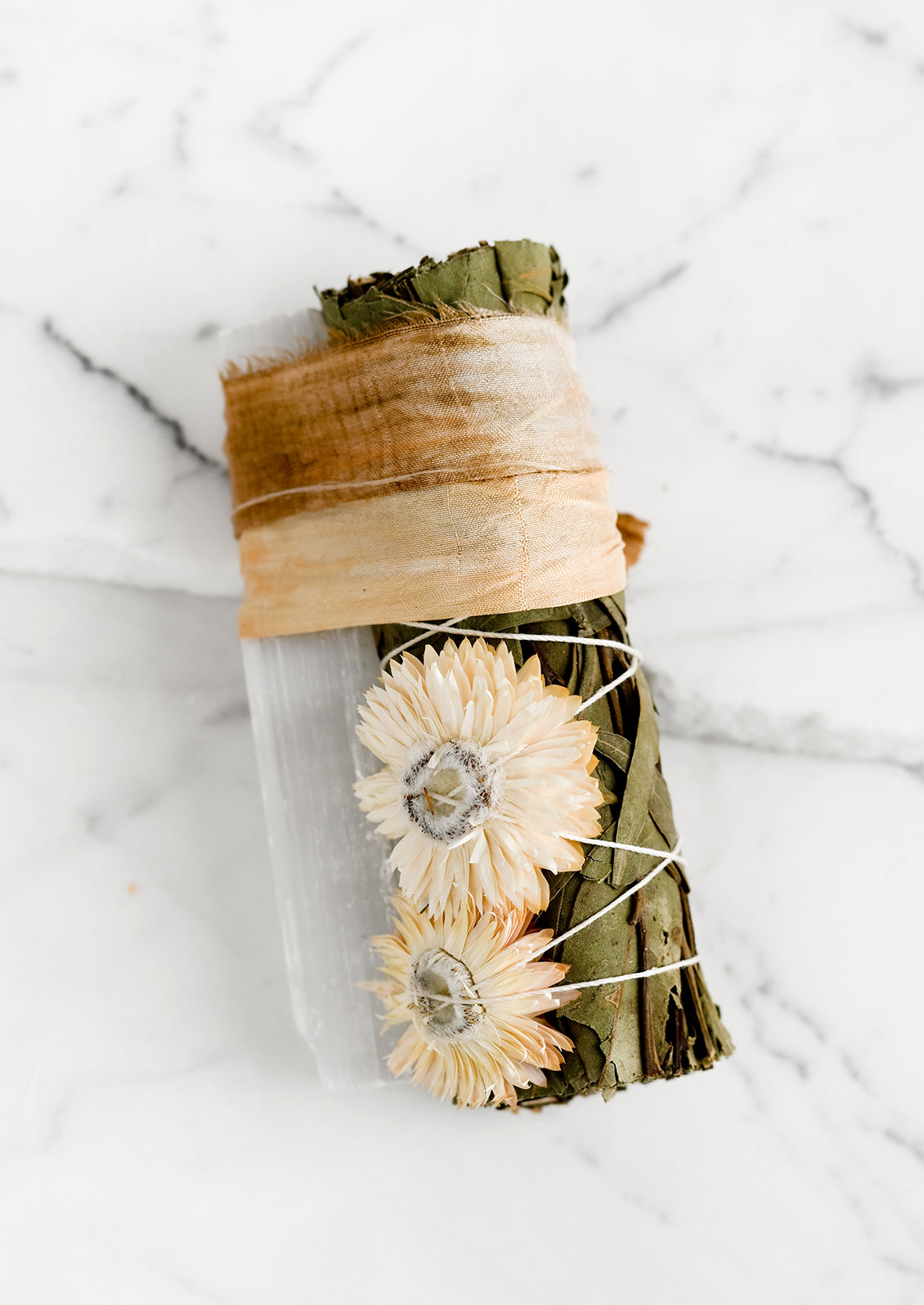 A eucalyptus and selenite smudge bundle bound with tan ribbon.