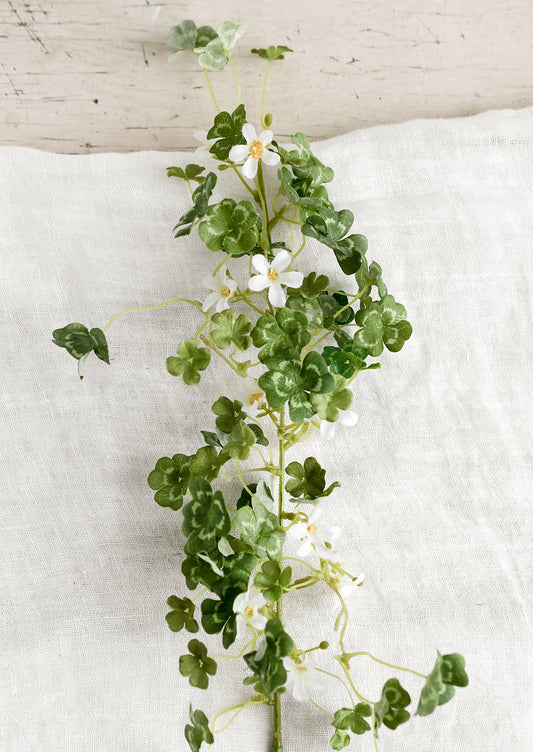 An artificial greenery stem of clover leaves with small white flowers.