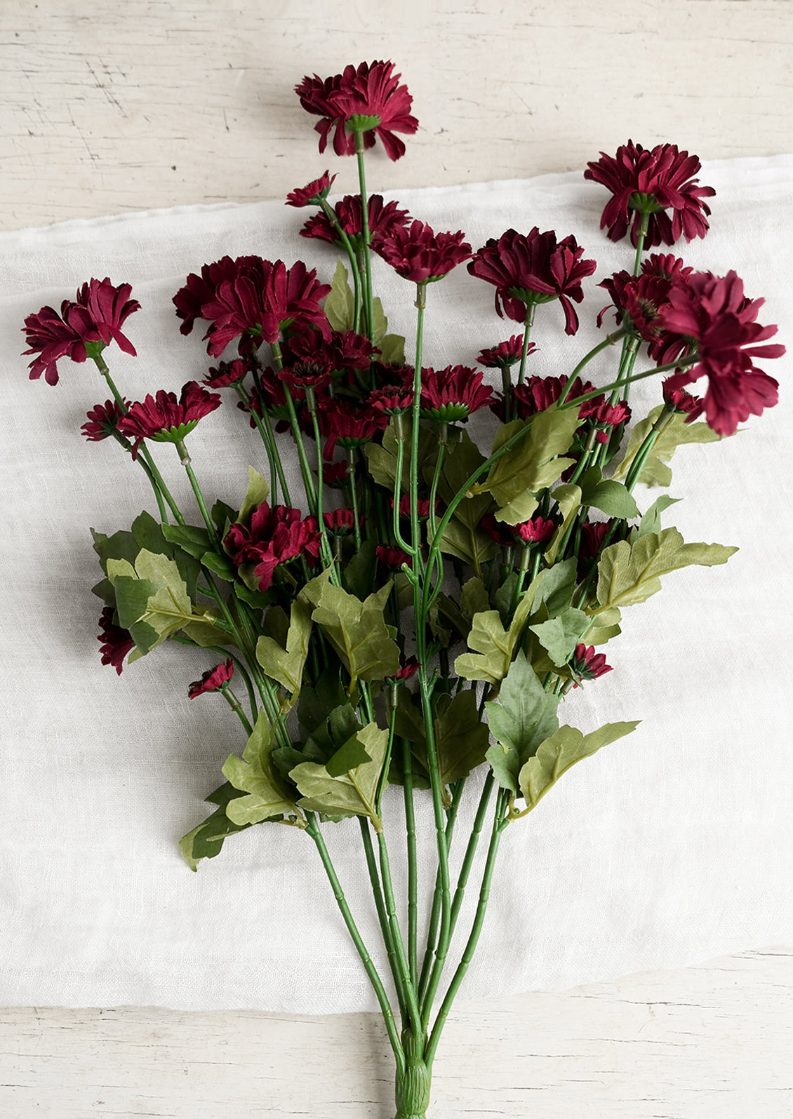 An artificial spray of small, burgundy gerbera flowers.