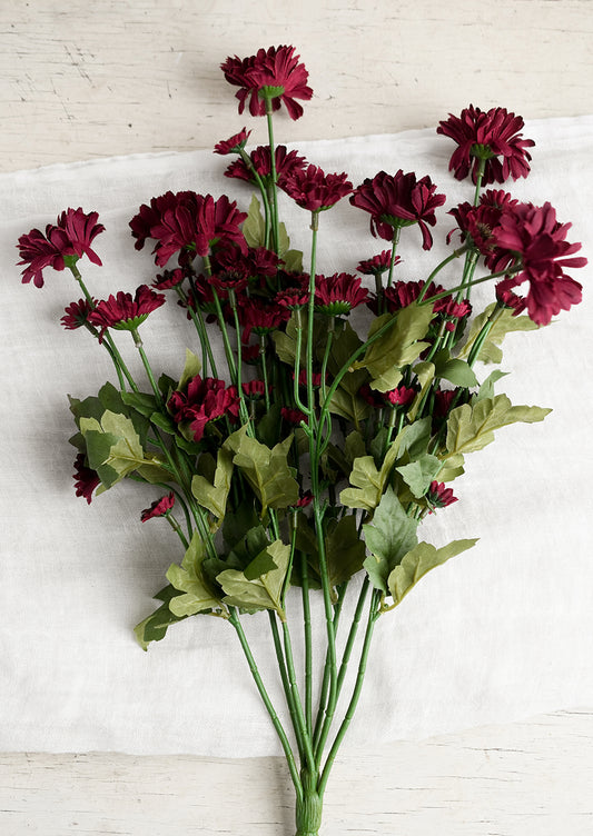 An artificial spray of small, burgundy gerbera flowers.