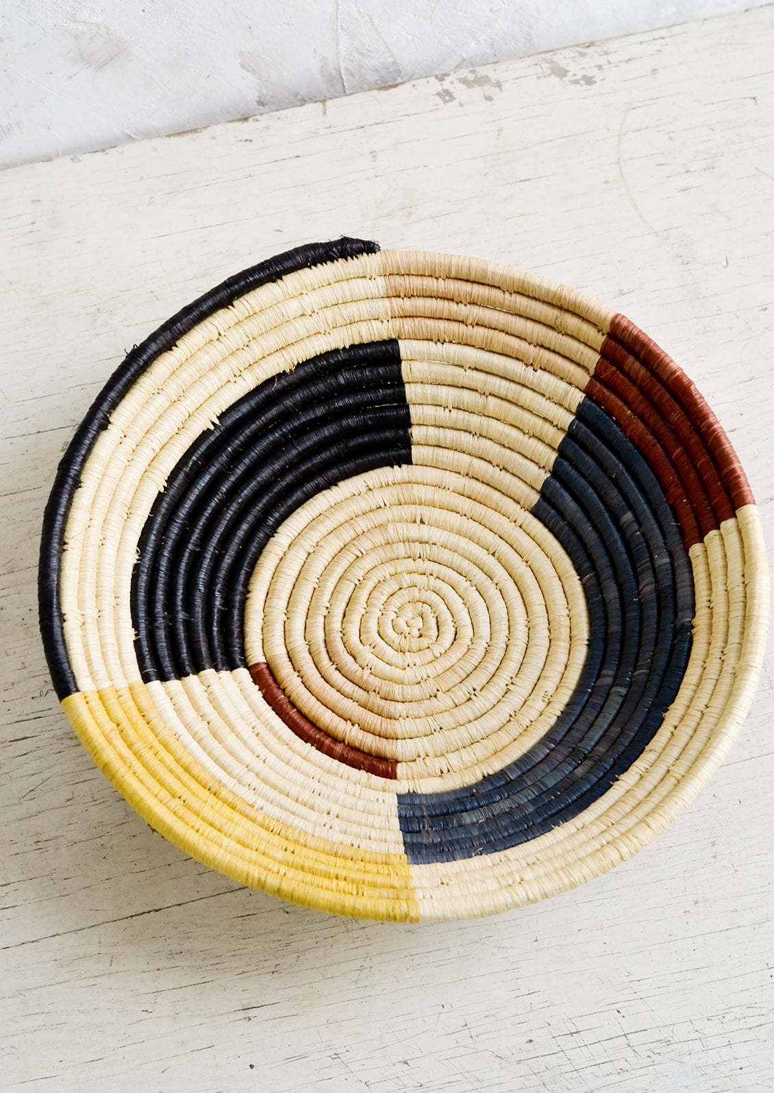 A round bowl made of raffia with a color blocked design in muted primary hues.