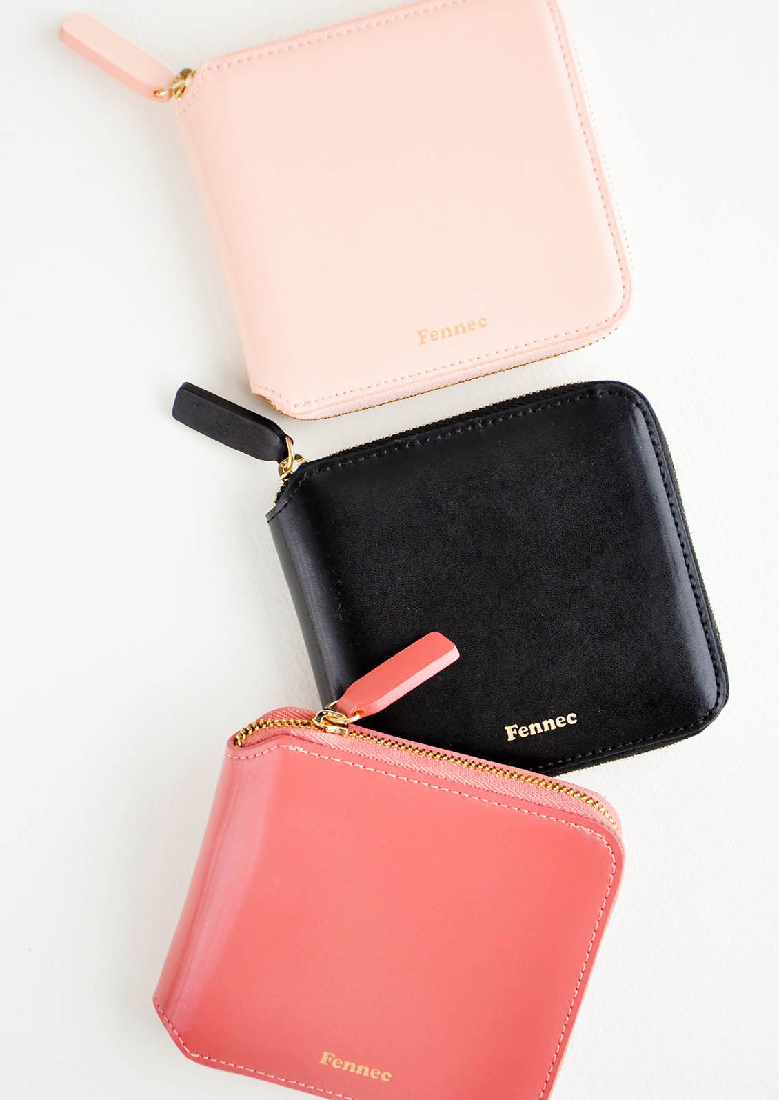 Three leather zip wallets in pale pink, black, and deep pink.