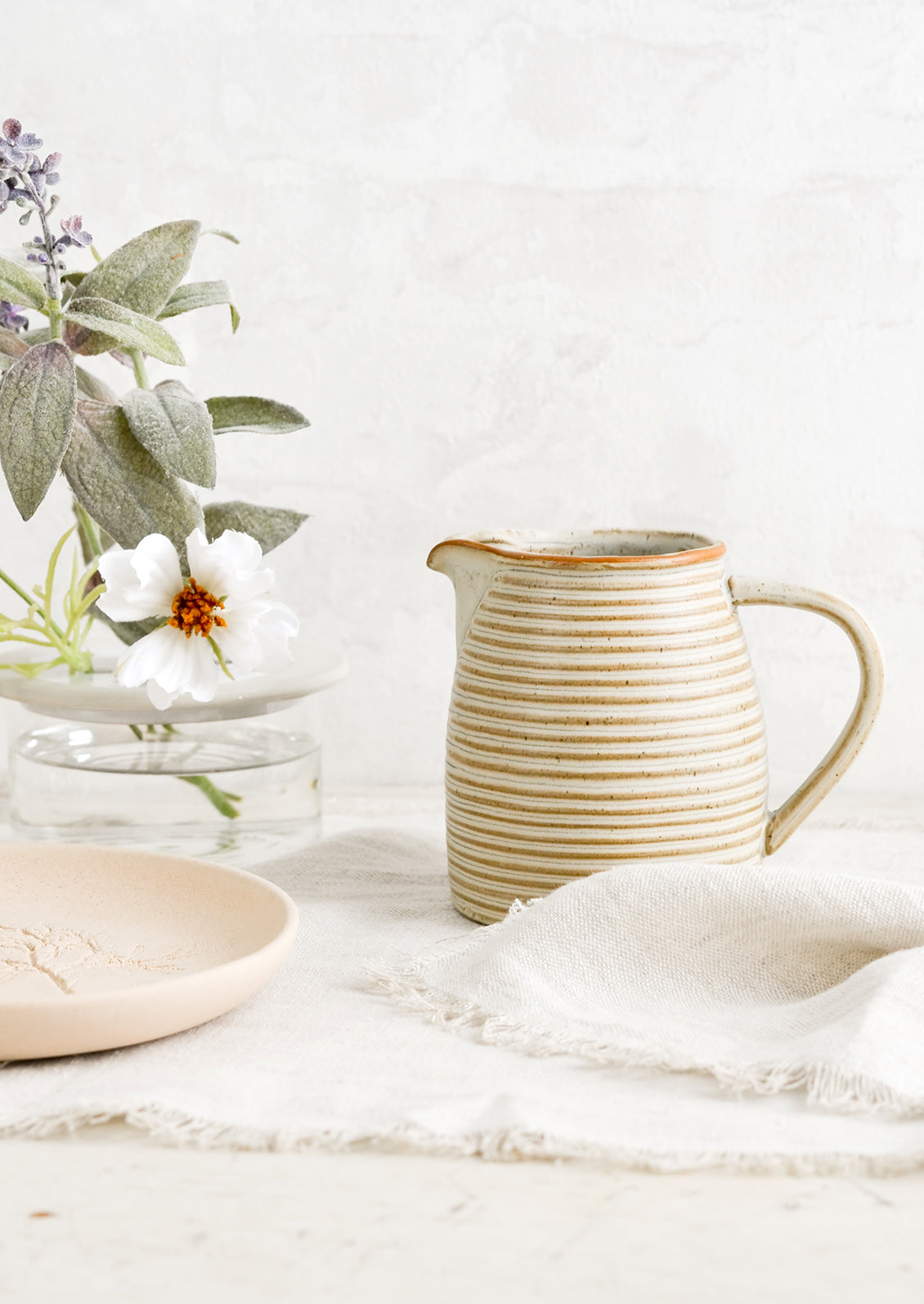 A tan ceramic pitcher with striped texture.