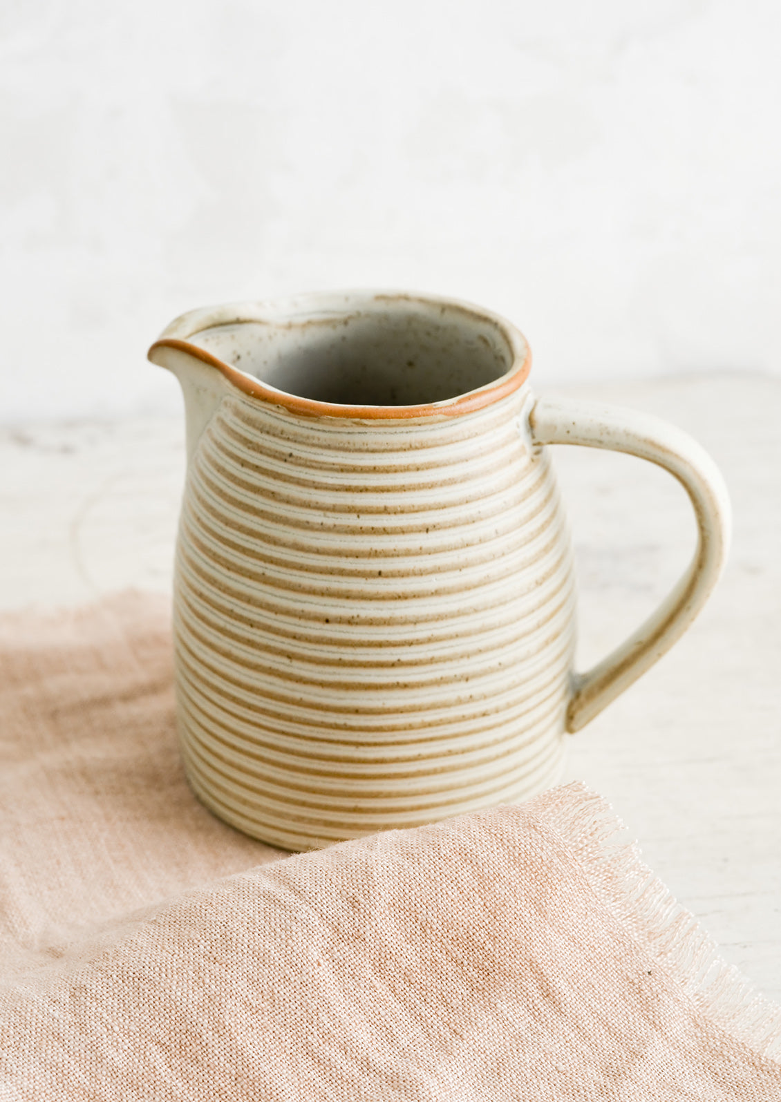 A ceramic pitcher on top of pink linen.