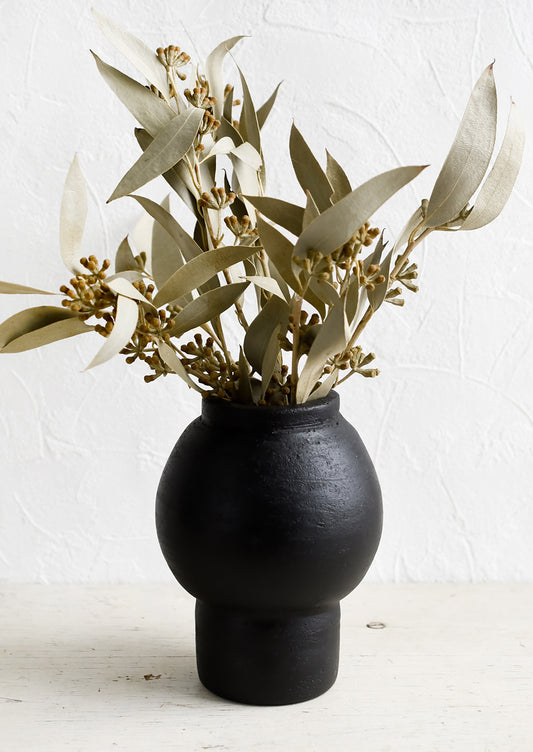 A shapely black vase with dried eucalyptus stems.