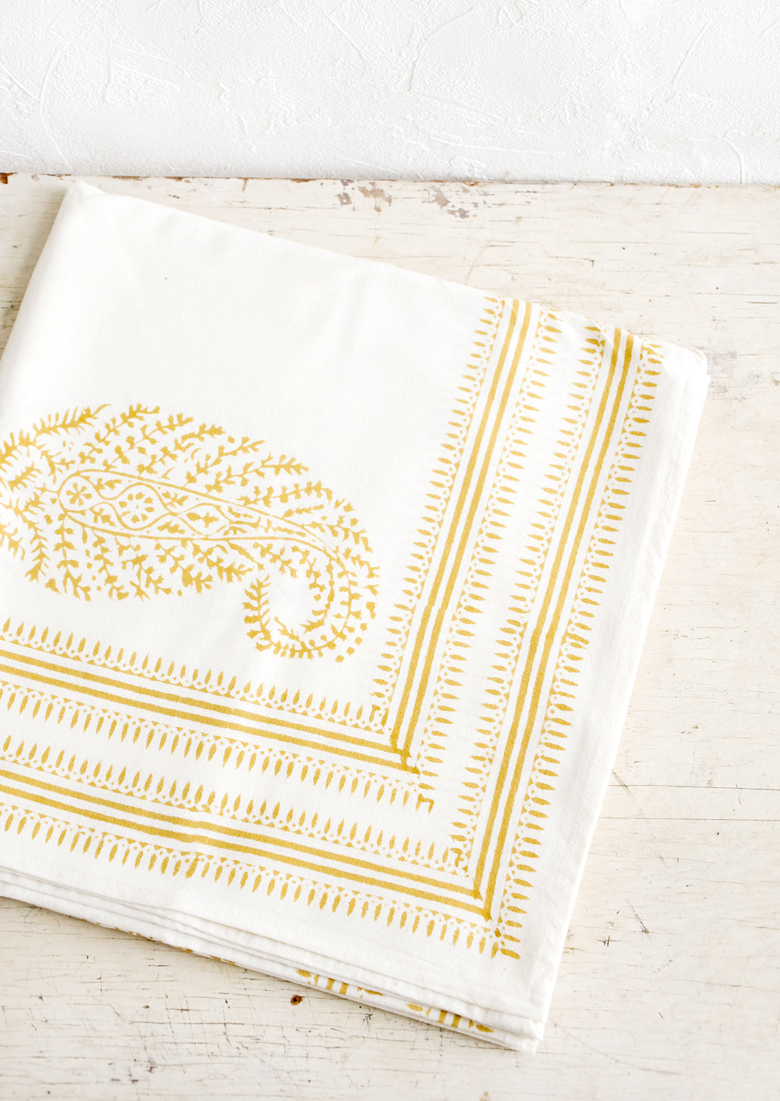 Folded white cotton tablecloth with mustard paisley pattern