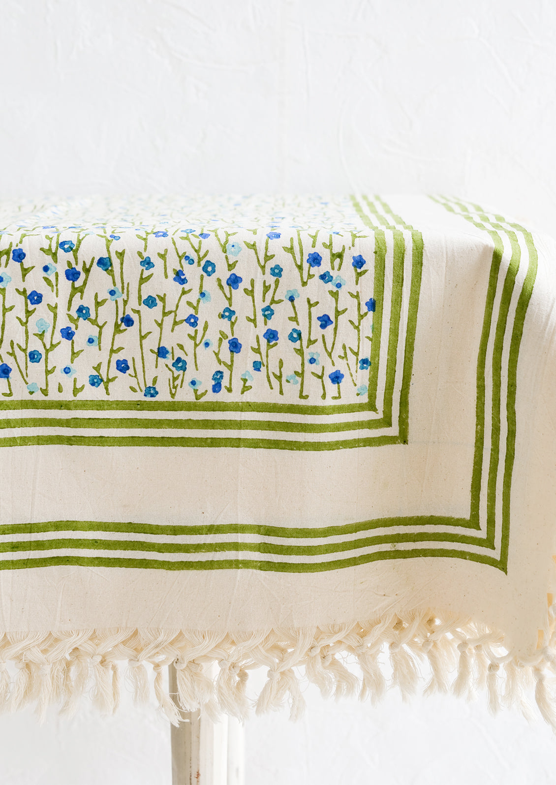 A floral block printed tablecloth with tassel trim, on a table.