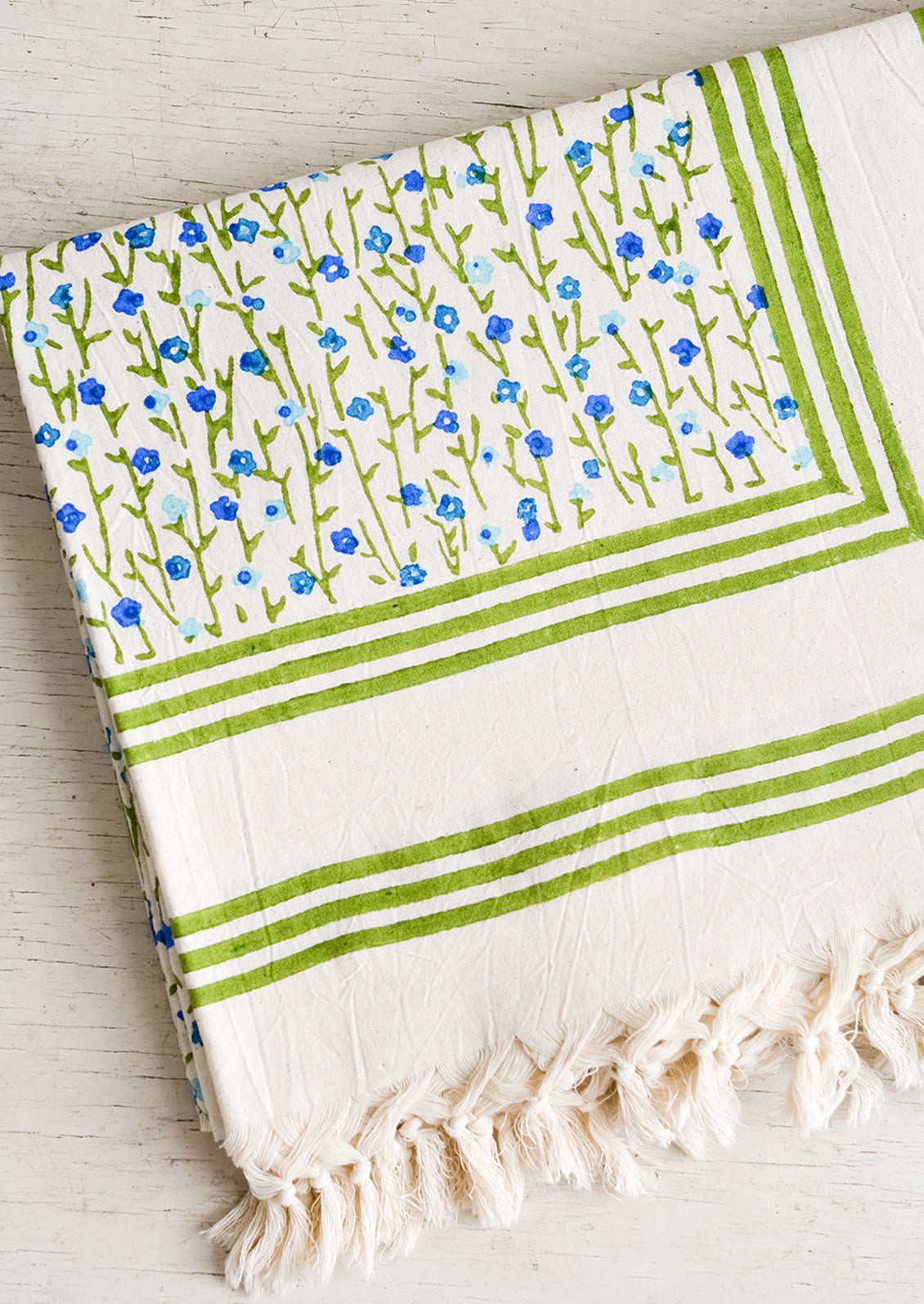 A folded cotton tablecloth with green border and green and blue floral pattern.