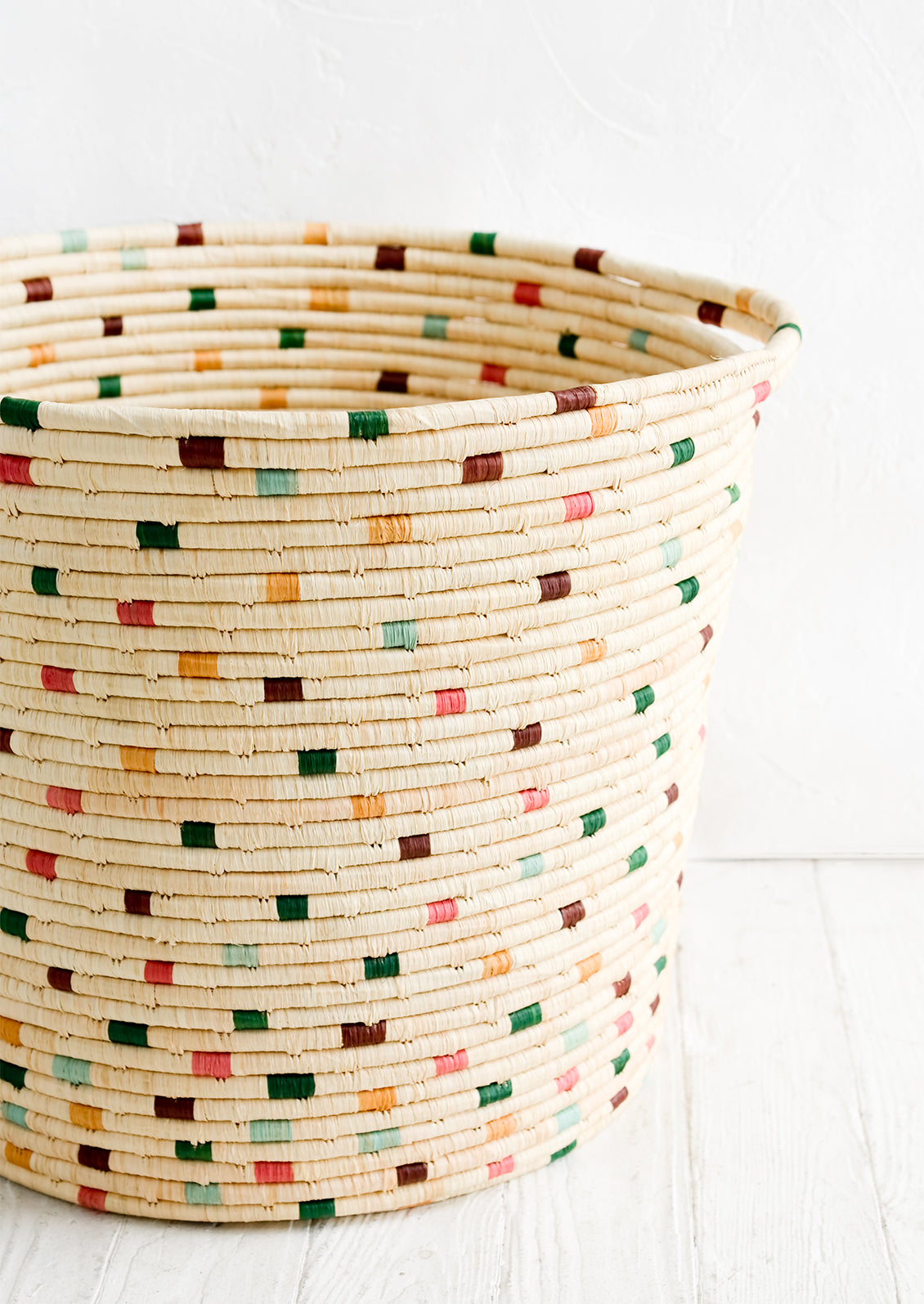 A round raffia hamper in natural with colorful dashes throughout.