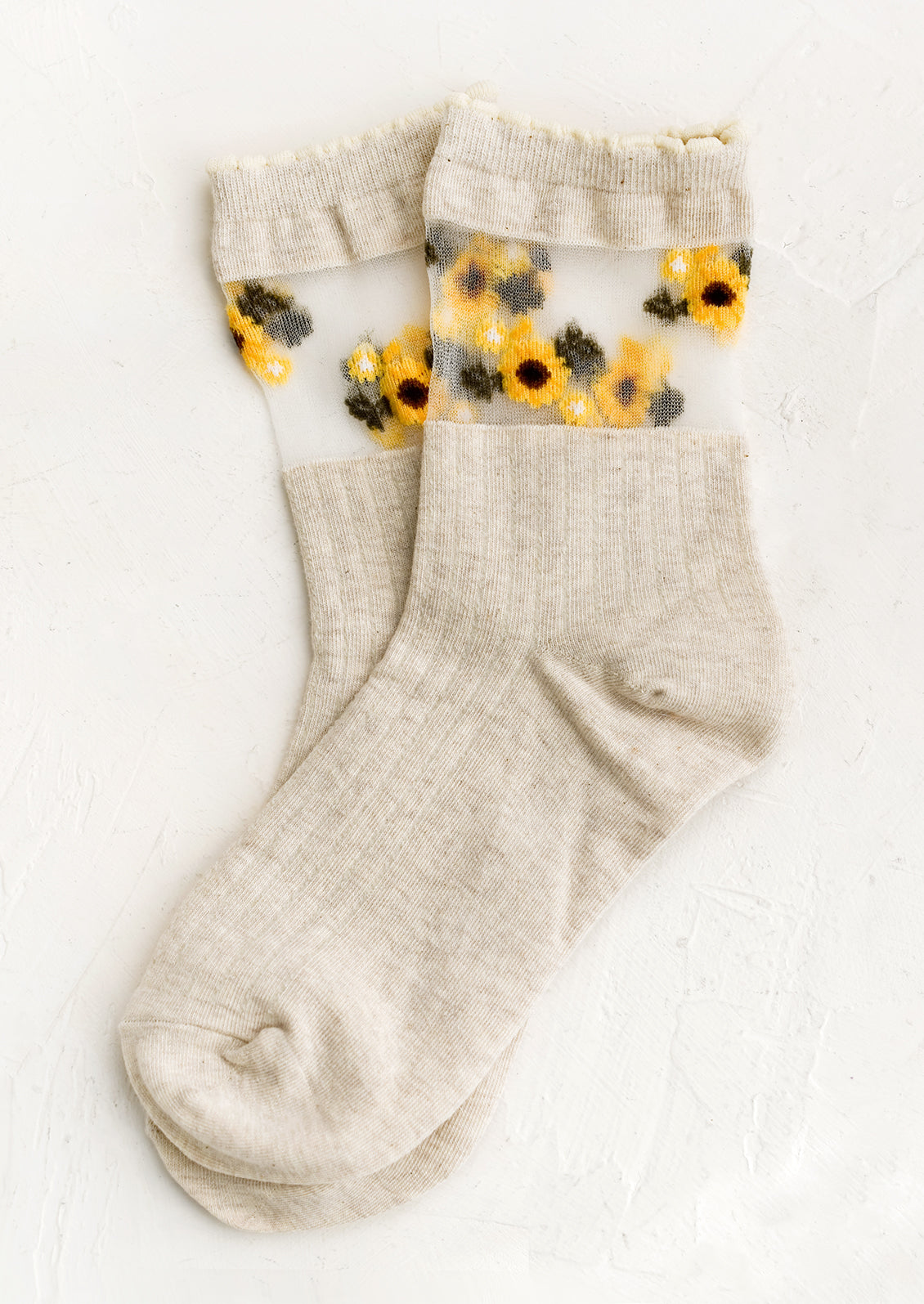 A pair of oatmeal colored socks with sheer mesh sunflower print band at ankle.