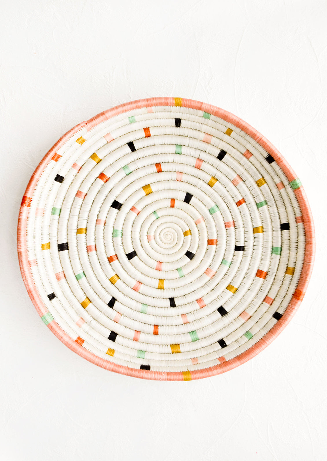 Round, shallow serving tray made from woven sweetgrass. Ivory with pastel colored dashes and peach rim.