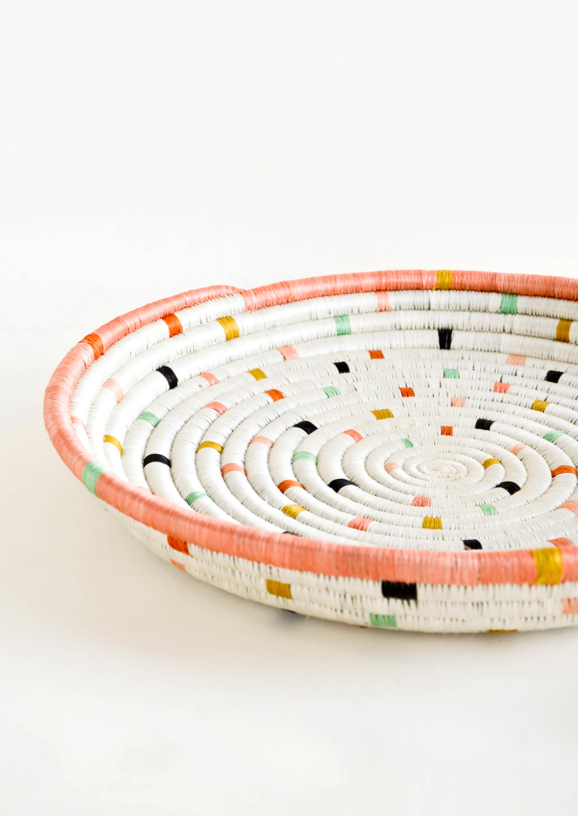Round, shallow serving tray made from woven sweetgrass. Ivory with pastel colored dashes and peach rim.