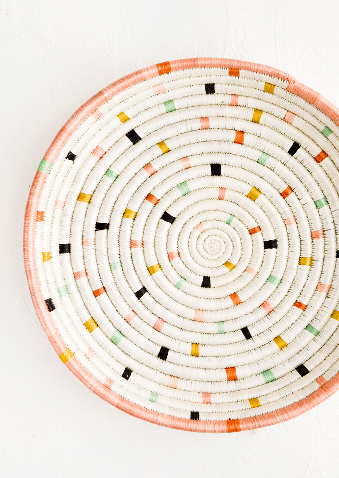 Round, shallow serving tray made from woven sweetgrass. Ivory with pastel colored dashes and peach rim.