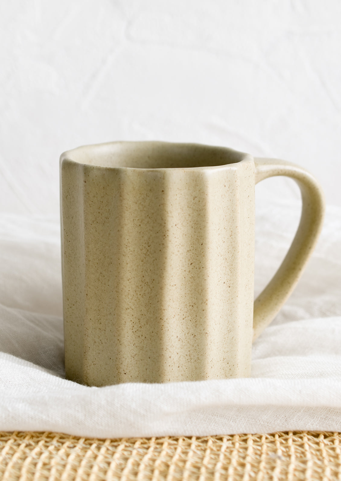 A fluted ceramic mug in sand.