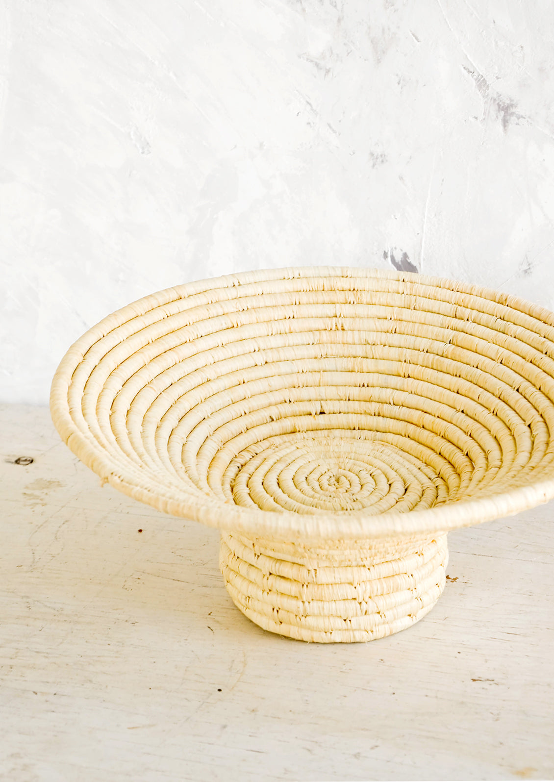 Footed pedestal bowl made from natural woven raffia, sitting on a table