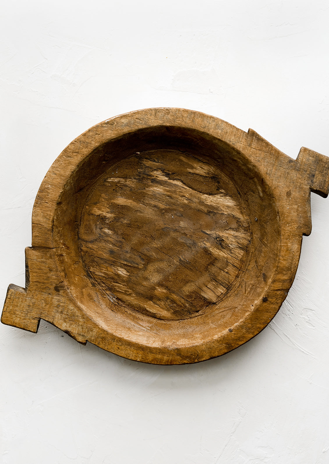 A round antique wooden tray with decorative side handles.