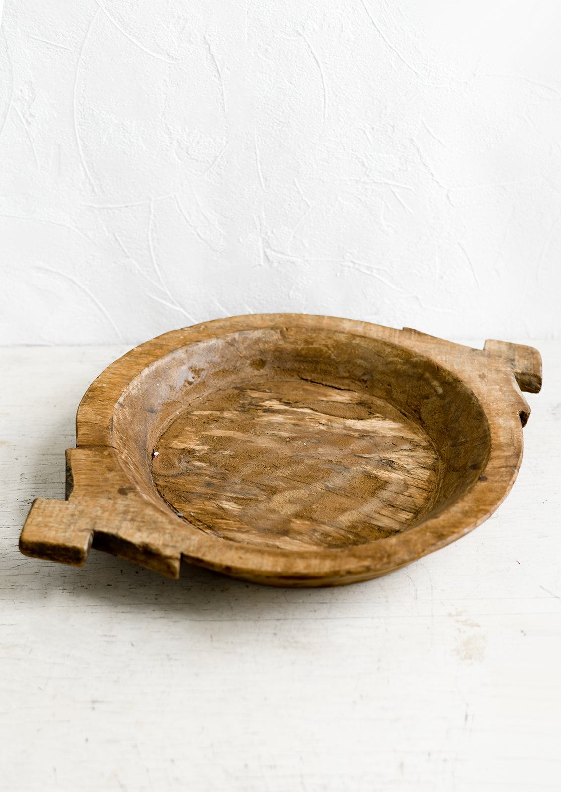 A round antique wooden tray with decorative side handles.