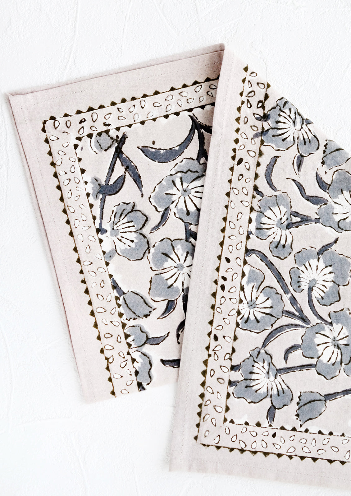 A block printed napkin in purple-grey color with bordered floral pattern.