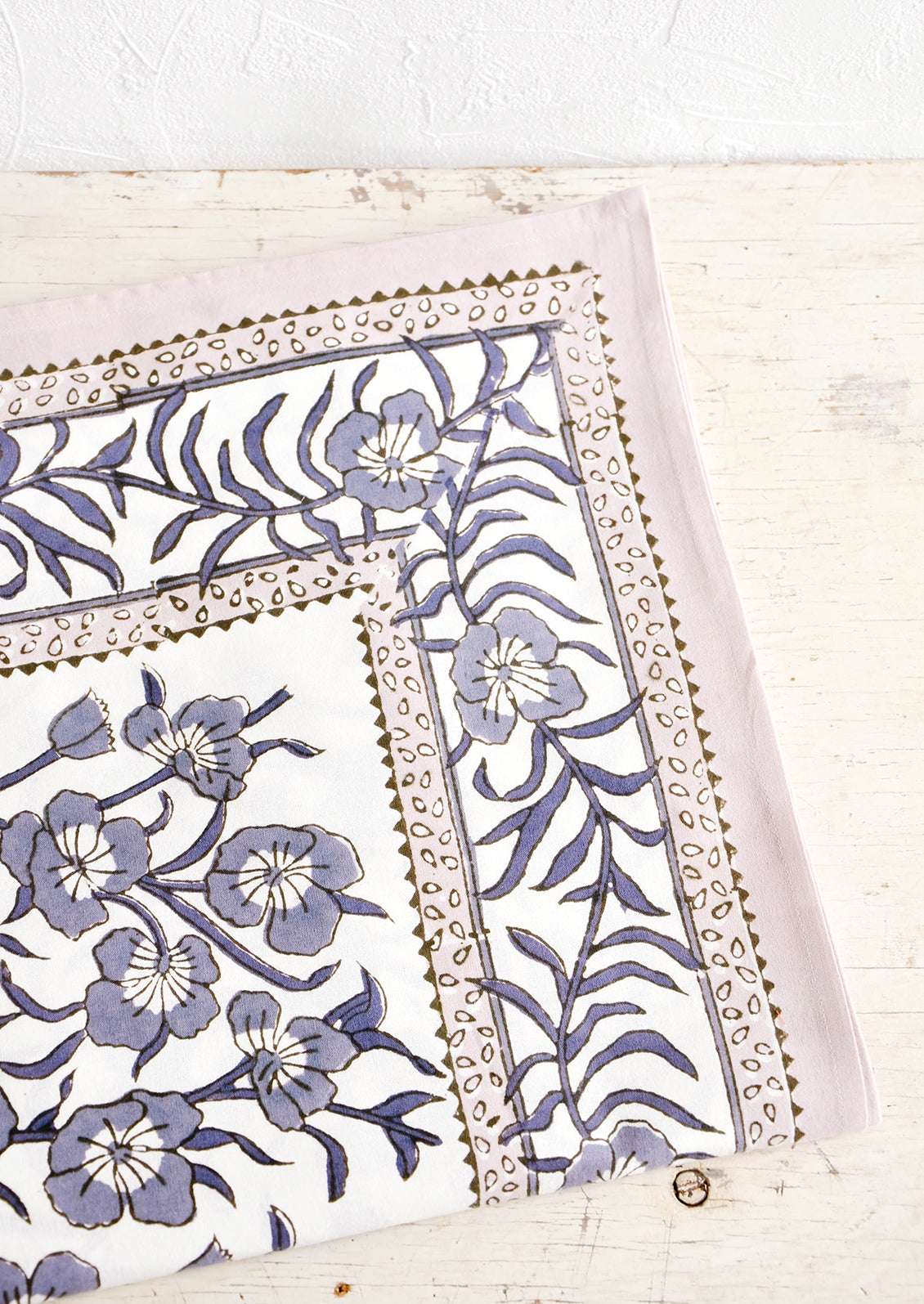 Tablecloth folded on a table. Features a bordered floral pattern in grey/lavender.
