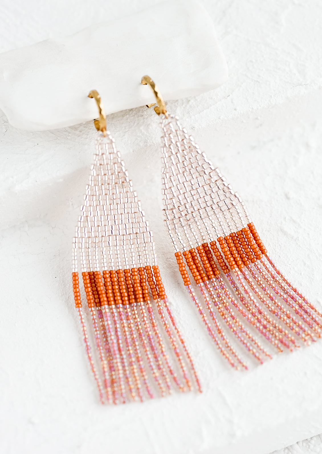 Beaded earrings featuring pink and rust beads layered into fringe, dangling from a gold hoop.