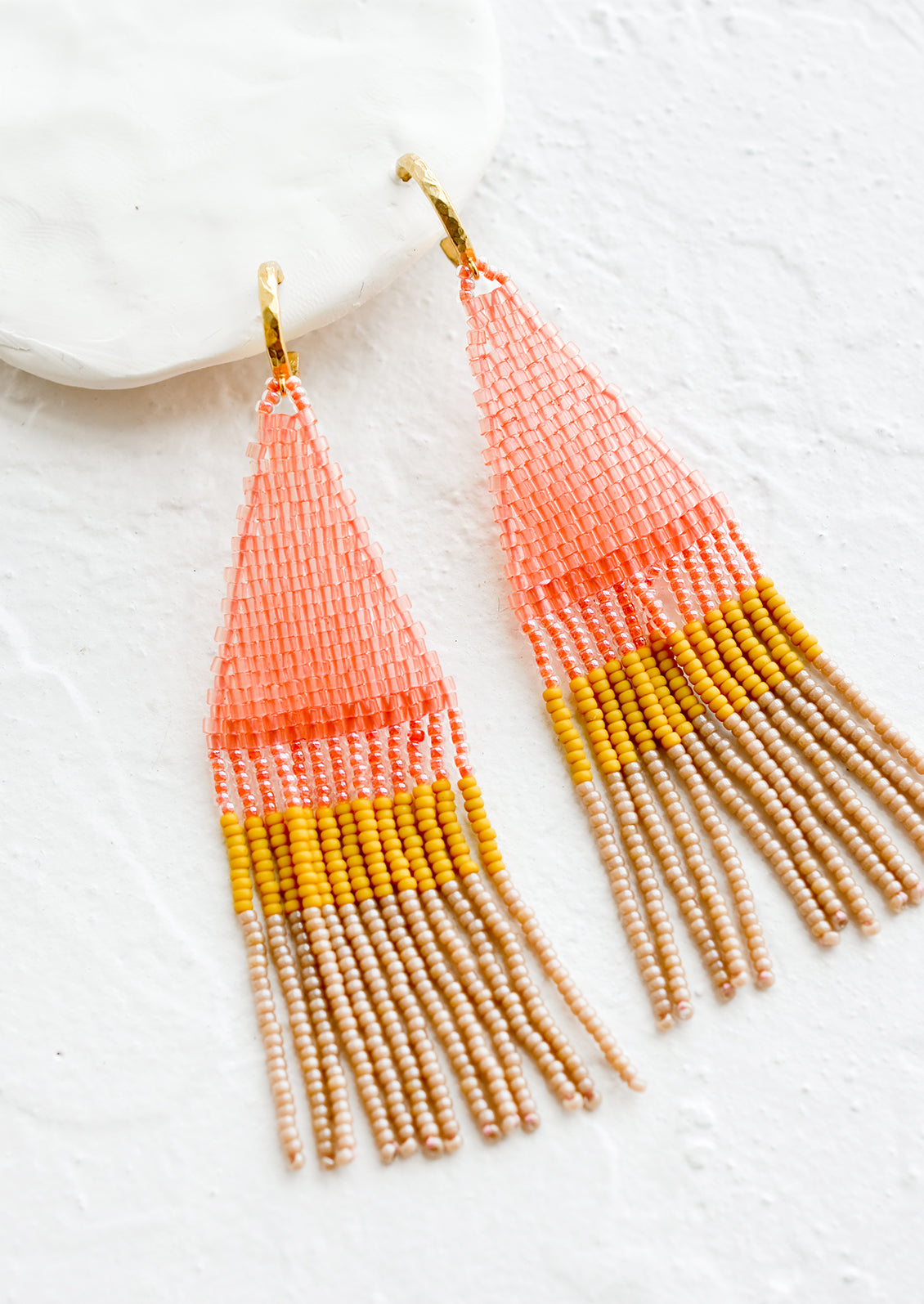 Beaded earrings featuring pink, yellow and brown beads layered into fringe, dangling from a gold hoop.