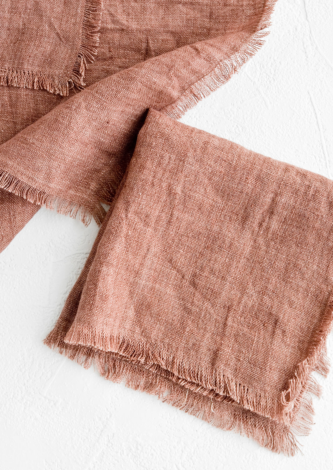 Folded currant colored linen napkins with frayed edges.