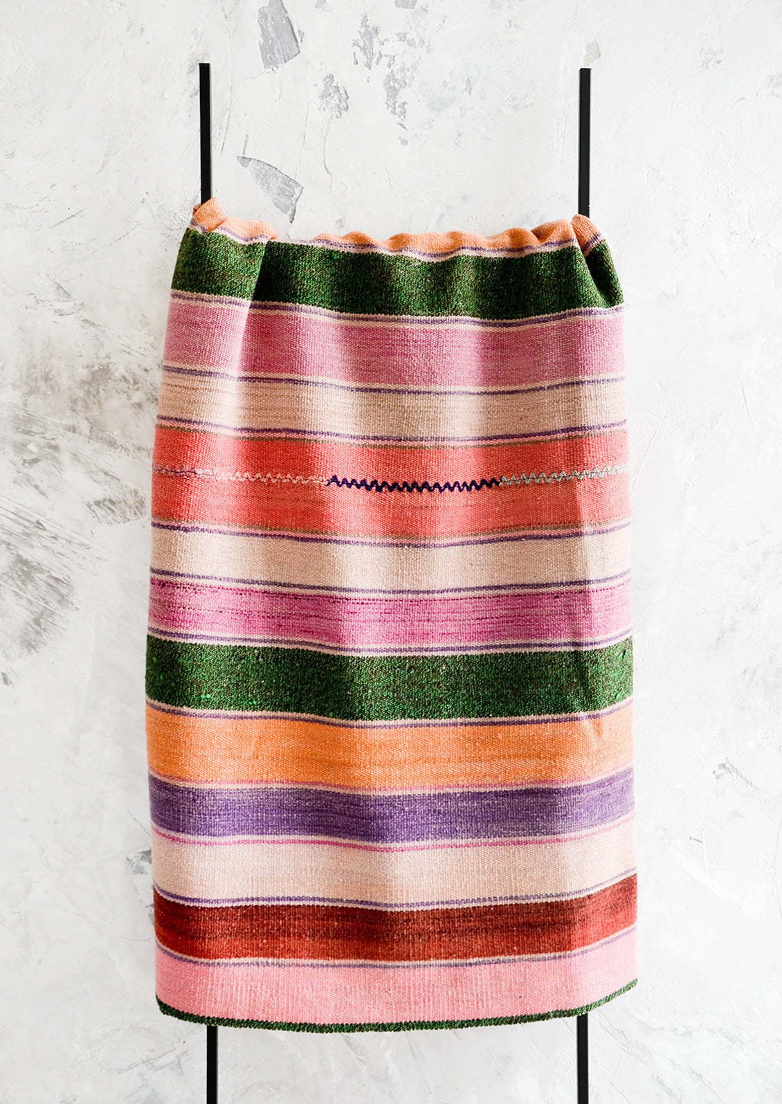 Colorful, striped woven textile intended for use as a rug or blanket, hung on a display ladder.
