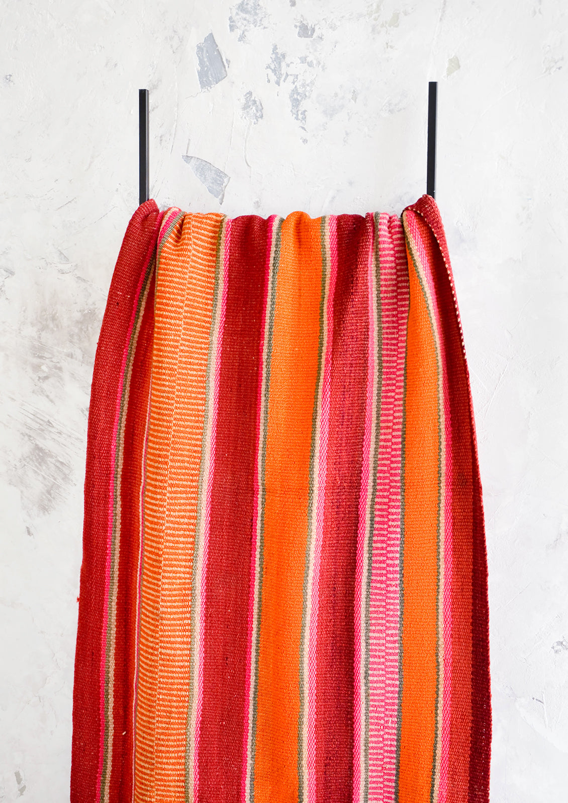 Colorful, striped woven textile intended for use as a rug or blanket, hung on a display ladder.