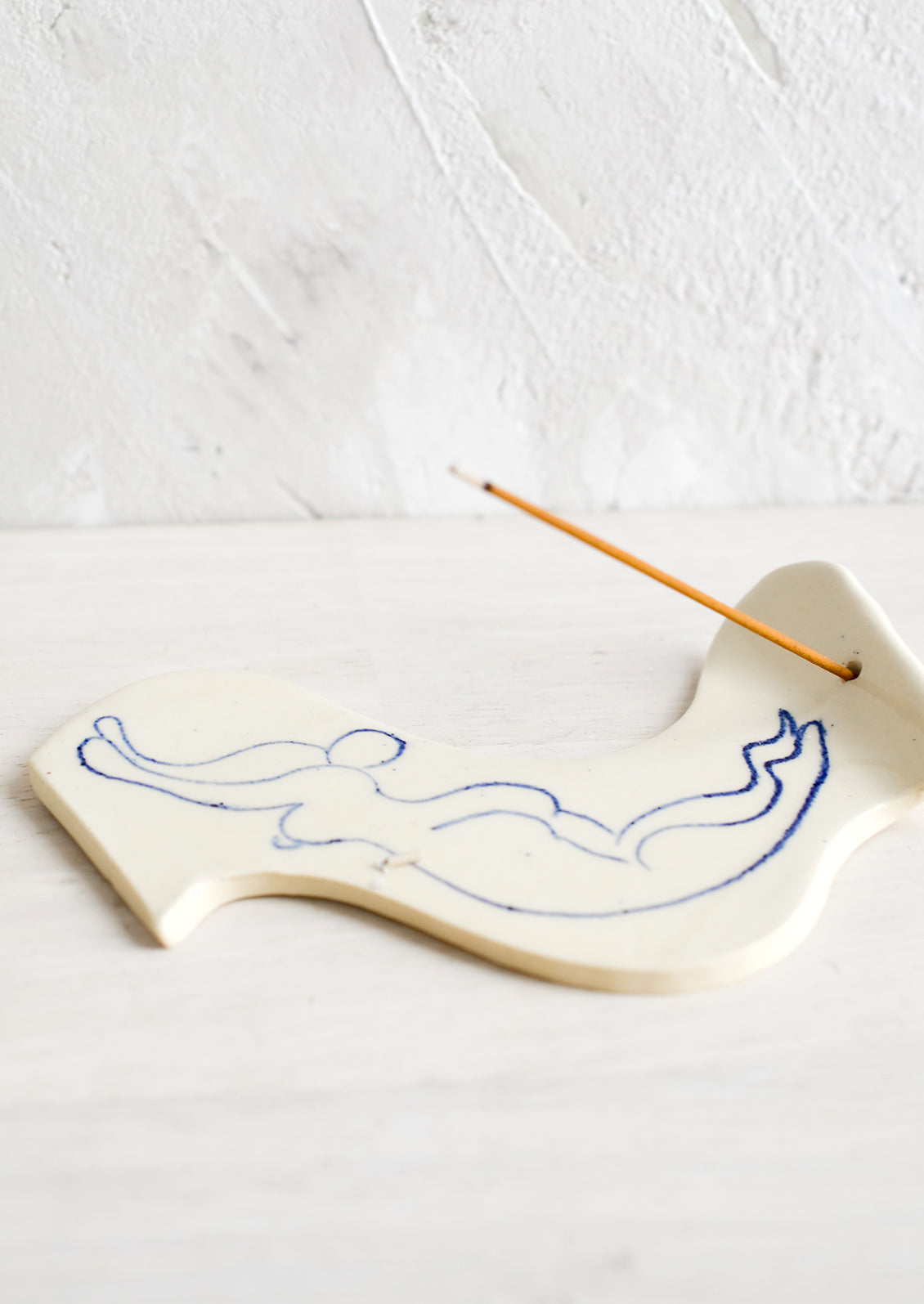 A ceramic incense holder with line drawn naked woman diving.
