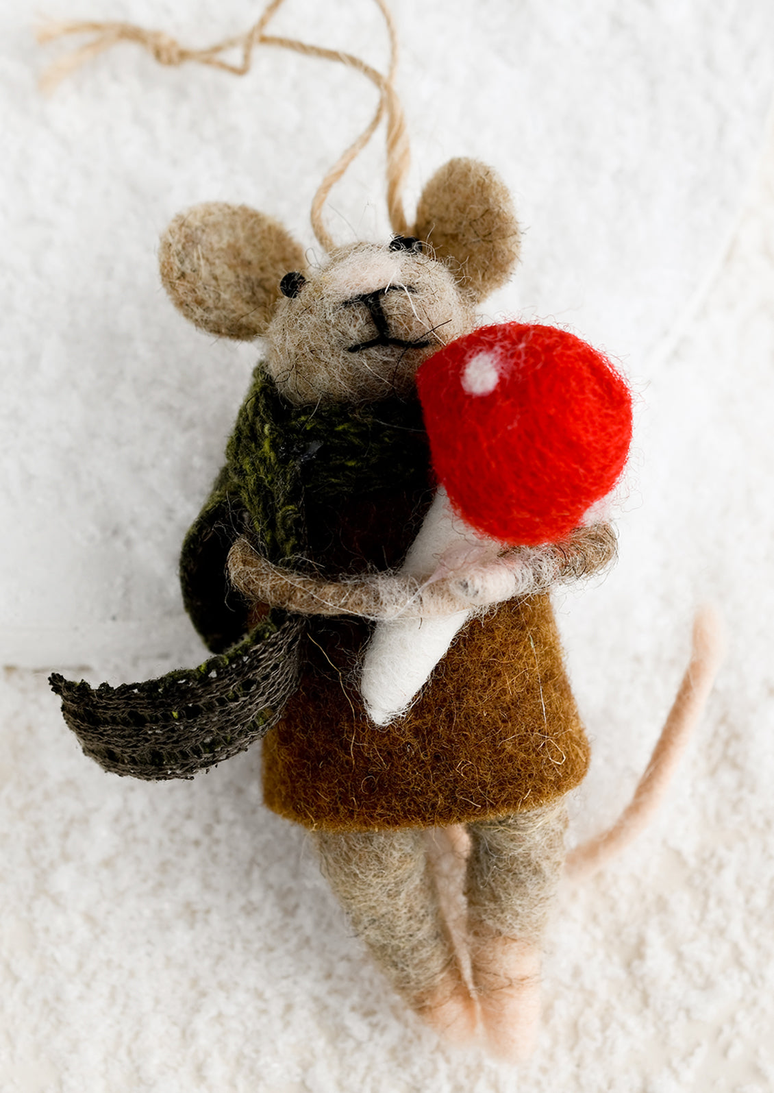 A felted mouse ornament wearing a scarf and holding a red mushroom.