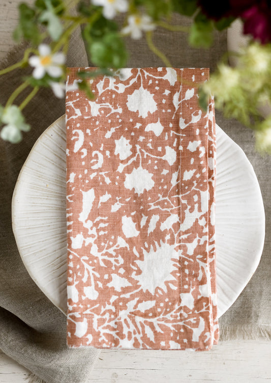 A botanical print linen napkin in clay brown with white pattern.