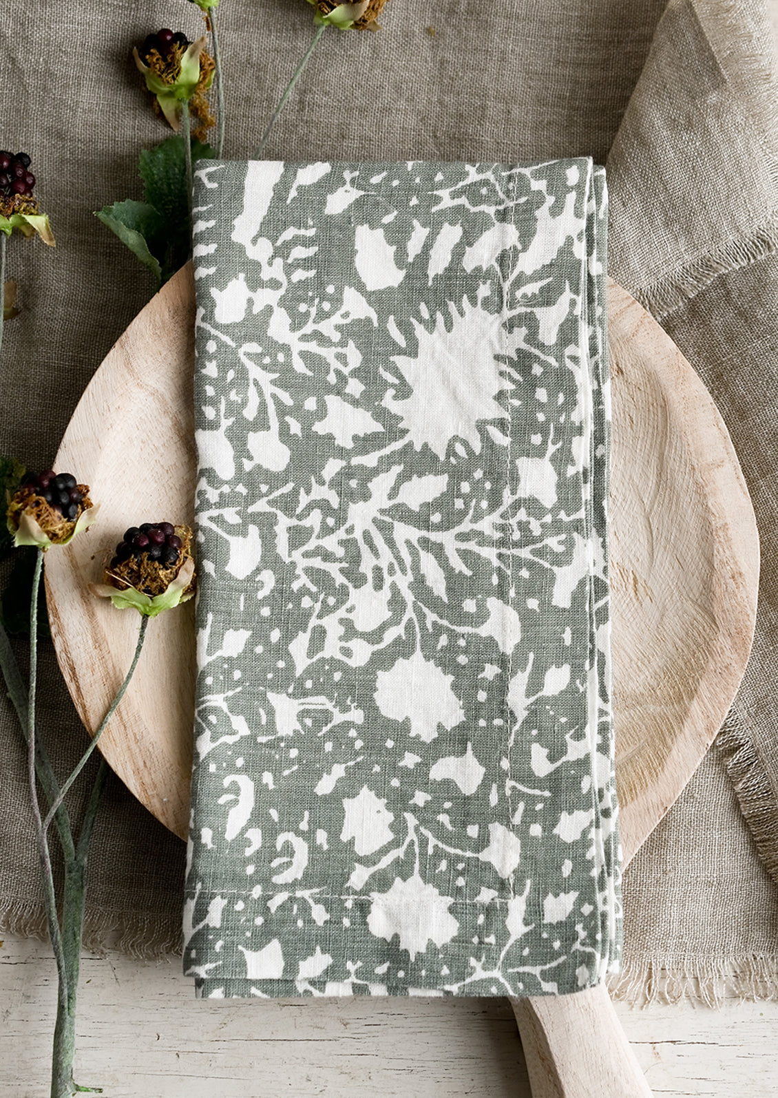 A botanical print linen napkin in sage green with white pattern.