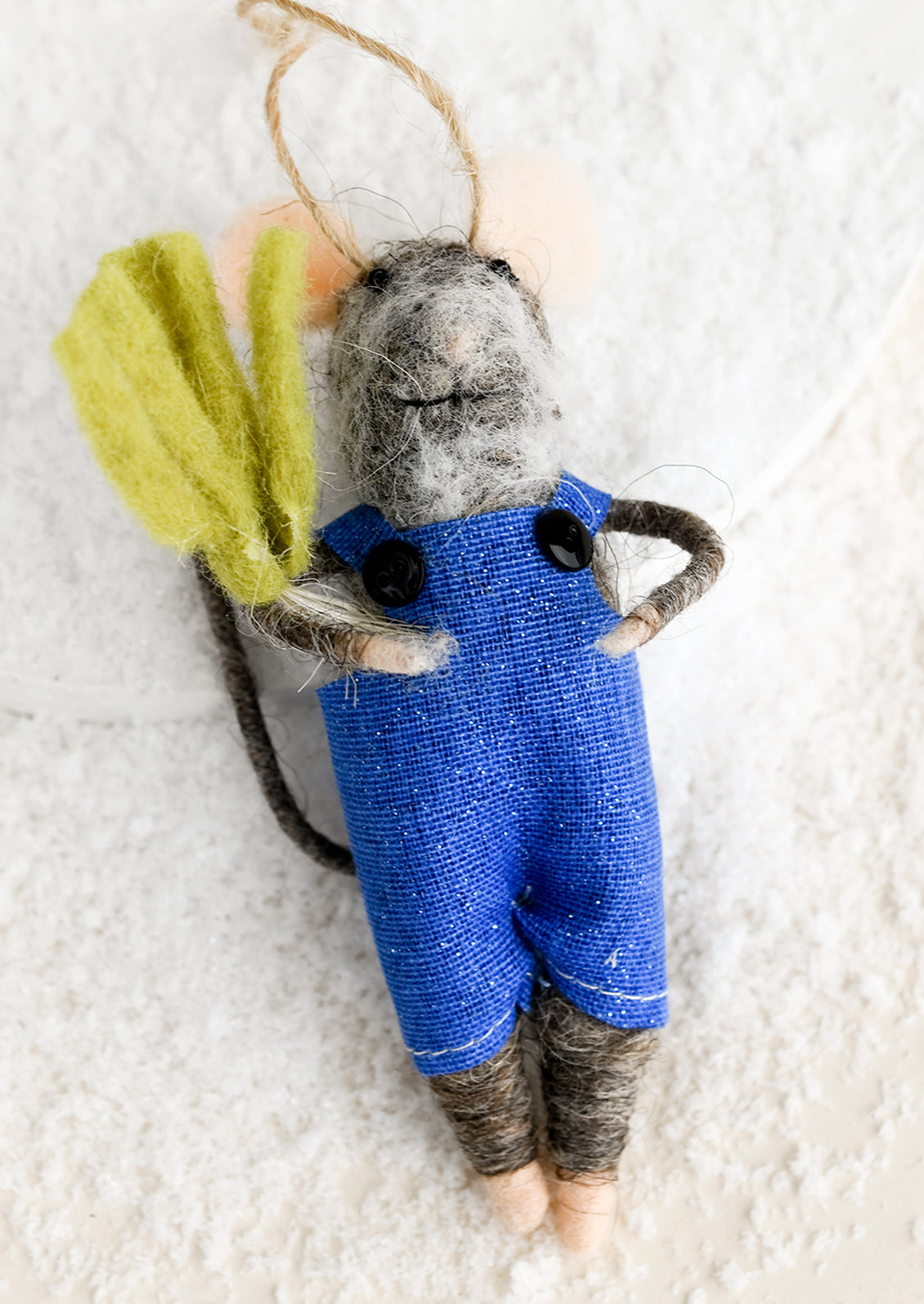 A felted mouse ornament wearing overalls and holding a green vegetable.