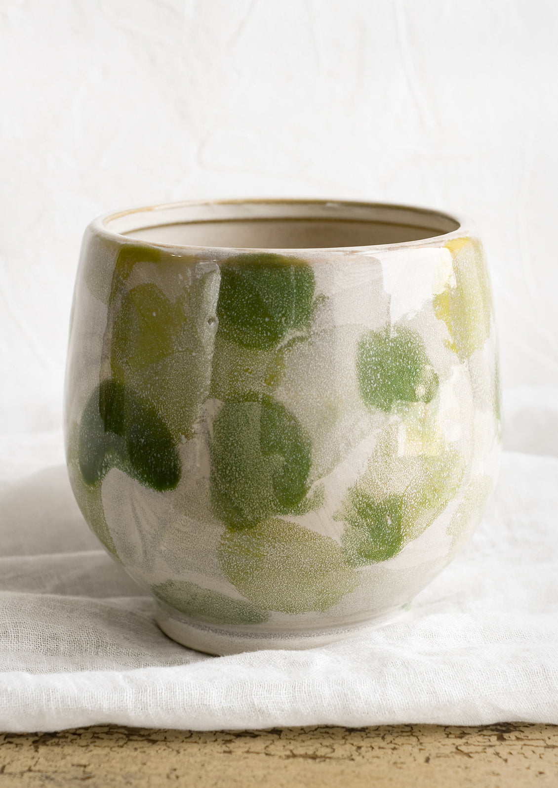 A footed planter with green paint stroke pattern.