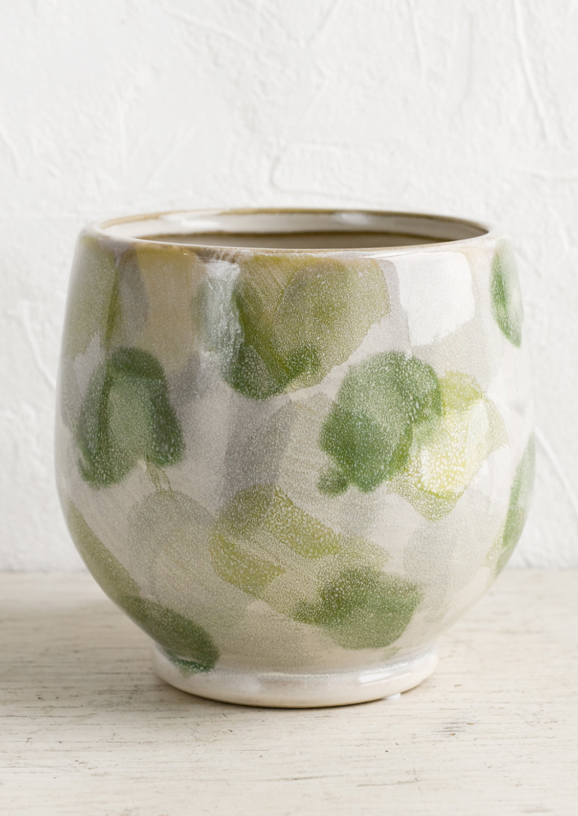 A footed planter with green paint stroke pattern.