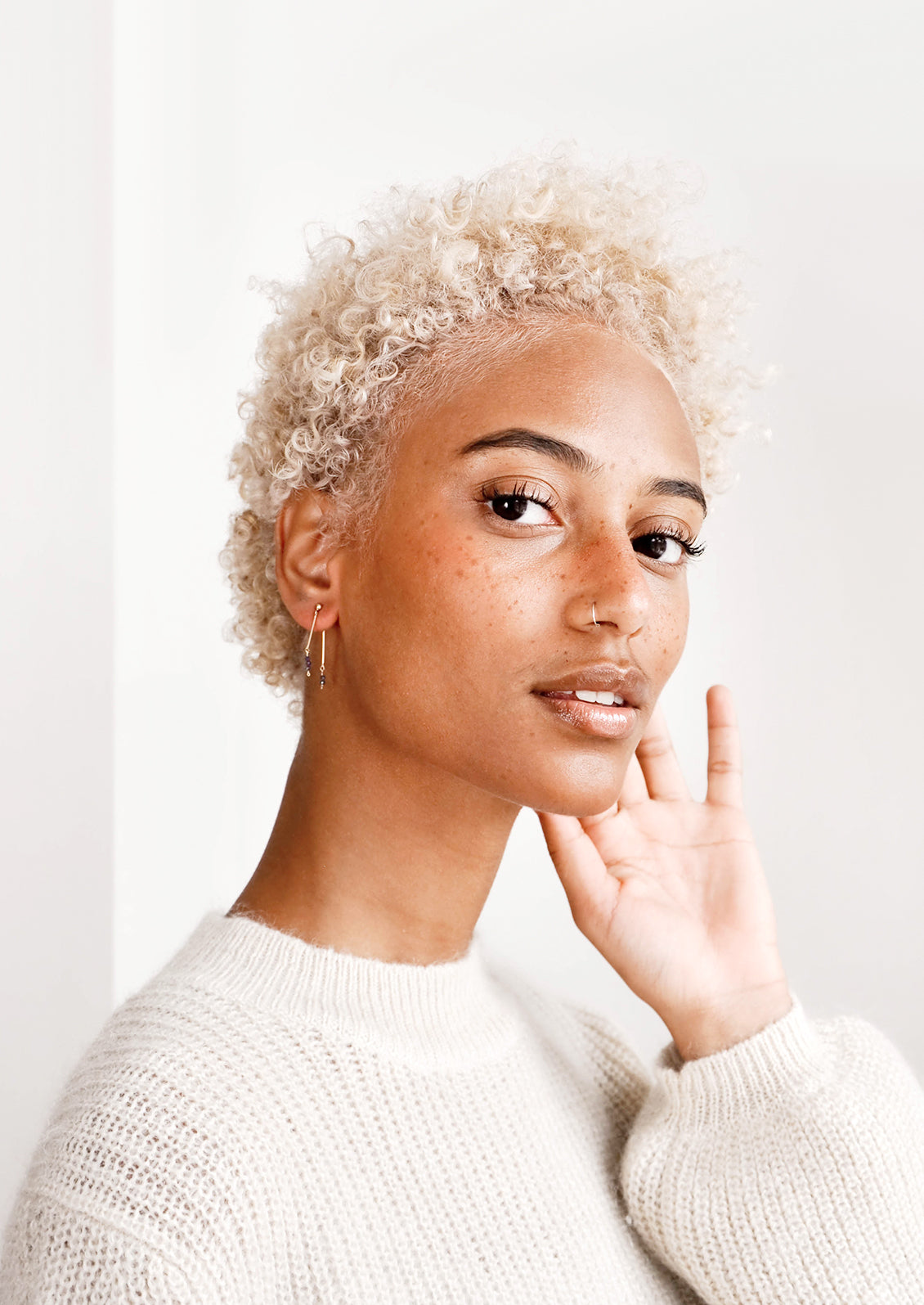 Model shot of woman wearing earrings and white top.